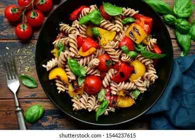 Whole wheat fusilli pasta with grilled vegetables in a black bowl on a wooden background. Top view with copy space.