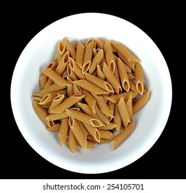 Whole Wheat Penne Pasta In A White Bowl On A Black Background.