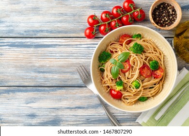 Weizenspaghetti-Teigwaren mit Brokkoli, Kirschtomaten und Basilikum in Schüssel auf Holzhintergrund. Draufsicht. Kopiert Platz.