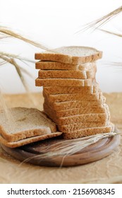 Whole wheat toast slices stacked with ears of rye on a round wooden board with parchment and a light gray background. Selective focus at shallow depth of field - Shutterstock ID 2156908345