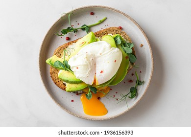 Whole wheat toasted bread with avocado, poached egg, pea sprouts and cheese over white background. Top view. Healthy diet breakfast