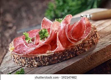 Wholegrain bread with seeds topped with spicy Italian salami sausage and parsley on an old grunge rustic wooden board