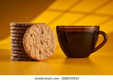 Wholegrain oat digestive biscuits and morning coffee with window shadow over yellow background