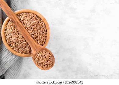 Wholegrain Uncooked Raw Spelt Farro In Wooden Spoon And Bowl On Grey Stone Table Background, Food Cereal Background, Copy Space, Top View