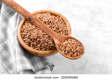 Wholegrain uncooked raw spelt farro in wooden spoon and bowl on grey stone table background, food cereal background, close up, top view
