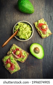 Wholemeal bread with avocado spread and prosciutto on wooden kitchen table
