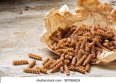 wholemeal pasta fusilli from organic whole grain spelt falling from a paper bag on a rustic wooden table, copy space