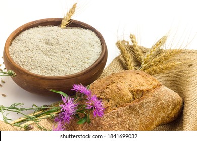 Wholemeal wheat flour in ceramic bowl, wheat ears, homemade bread and cornflowers on  sackcloth isolated on white background