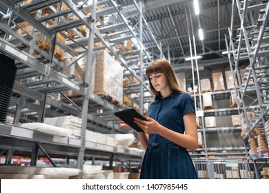 Wholesale warehouse. Beautiful young woman worker of store in shopping center. Girl looking for goods with a tablet is checking inventory levels in a warehouse. Logistics concept - Powered by Shutterstock