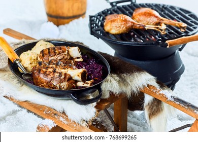 Wholesome grilled pork hocks with dumplings from a winter barbecue served with red cabbage in a pan on a bed of fresh snow