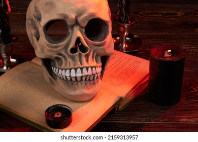 Wicca Satanic Ritual Concept. Humans Skull On The Satanic Bible Book. Extinguished Candels Indoors. The End Of The Show.