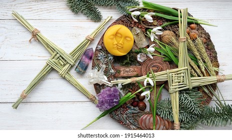 Wiccan altar for Imbolc sabbat. winter-spring pagan festive ritual. Brigid's cross, crystals, wheel of the year, snowdrops, sun and moon symbol on wooden table. Imbolc holiday, spring equinox.