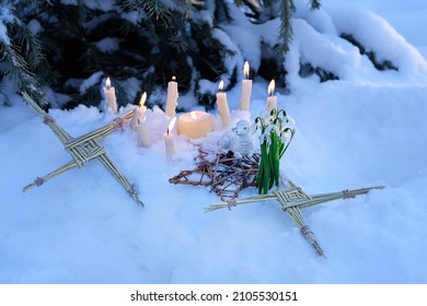 Wiccan altar for Imbolc sabbath, pagan holiday ritual. Brigid's cross of straw, candles, snowdrops, toy sheep on snow, winter forest natural background. symbol of Imbolc holiday, spring equinox