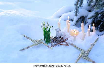 Wiccan altar for Imbolc sabbath, pagan holiday ritual. Brigid's cross of straw, candles, snowdrops, toy sheep on snow, winter forest natural background. symbol of Imbolc holiday, spring equinox.