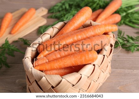 Wicker basket and board with fresh carrots on wooden table