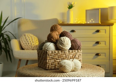 Wicker basket with colorful yarns and knitting needles on coffee table in cozy room - Powered by Shutterstock