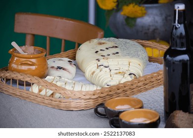 A wicker basket containing various types of sliced cheese, a jar of honey, and two ceramic cups on a table. - Powered by Shutterstock