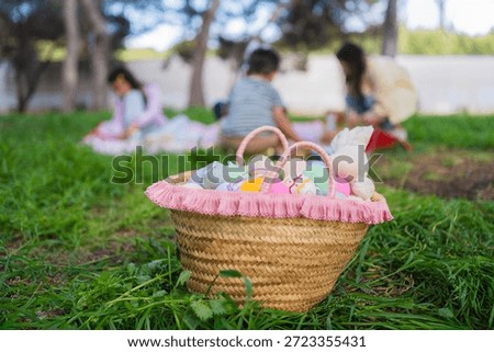 Wicker basket filled with decorated easter eggs and bunny toy on green grass with blurred family in background