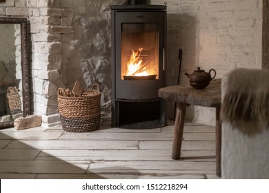 Wicker basket with firewood near fire chimney. Wood stove fireplace with metal body and glass door in comfort house with cozy interior in room