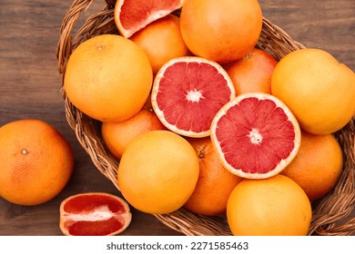 Wicker basket with fresh grapefruits on wooden table, flat lay