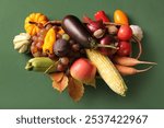 Wicker basket with fresh vegetables, fruits and autumn leaves on green background. Harvest festival