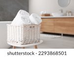 Wicker basket with fresh white towels on stool in bathroom. Space for text