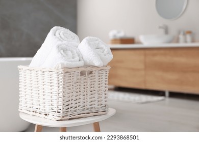 Wicker basket with fresh white towels on stool in bathroom. Space for text