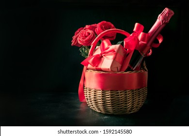 Wicker Basket With Gift, Bouquet Of Red Roses, Bottle Of Champagne On Black Table. Close Up. Horizontal Format. Space For Wishes. Gift Baskets And Flower Deliveries.