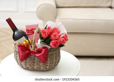 Wicker basket with gift, bouquet and wine on white table indoors. Space for text - Shutterstock ID 1915334365