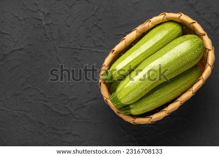 Wicker basket with many fresh green zucchini on black background