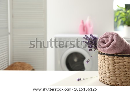 Wicker basket with rolled clean towel and lavender flowers on white table indoors. Space for text