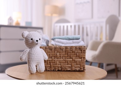 Wicker basket with stack of child's clothes and toy bear on coffee table indoors, closeup