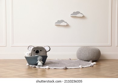 Wicker basket, toys and pouf near white wall indoors. Interior design