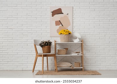 Wicker baskets with chrysanthemum flowers and home decor on shelving unit near chair against white brick wall - Powered by Shutterstock