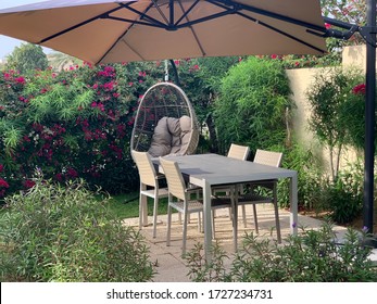 Wicker Furniture, Outdoor Chair Set, Table, Hanging Chair And Beige Umbrella In The Garden. Outdoor Dining Area