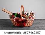 Wicker gift basket with sparkling wine and Christmas decor on grey textured table