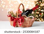 Wicker gift basket with wine and Christmas decor on light table