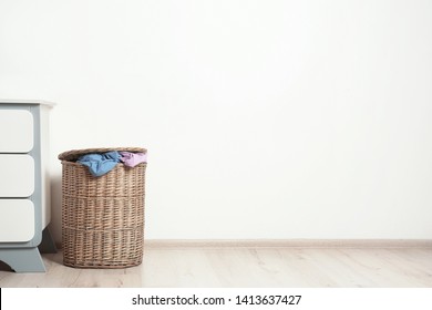 Wicker laundry basket with dirty clothes on floor near wall. Space for text