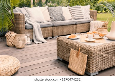 Wicker patio set with beige cushions standing on a wooden board deck. Breakfast on a table on a backyard porch.