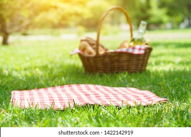 Wicker Picnic Basket With Food And Red Checkered Tablecloth On The Grass In A Park. Summer Picnic Background Concept.