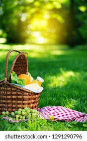 Wicker Picnic Basket With Healthy Food On Red Checkered Table Cloth On Green Grass Outside In Summer Park, No People