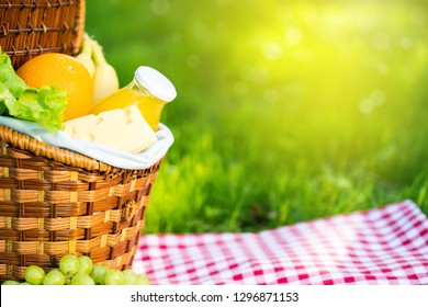 Wicker Picnic Basket With Healthy Food On Red Checkered Table Cloth On Green Grass Outside In Summer Park, No People