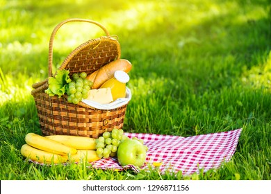 Wicker Picnic Basket With Healthy Food On Red Checkered Table Cloth On Green Grass Outside In Summer Park, No People