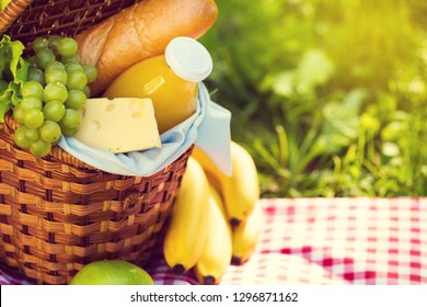 Wicker Picnic Basket With Healthy Food On Red Checkered Table Cloth On Green Grass Outside In Summer Park, No People