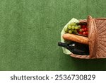 Wicker picnic basket with tasty food and bottle of wine on green grass background