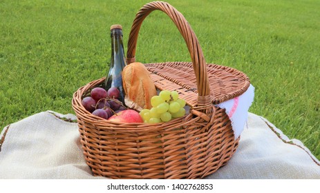 
Wicker Picnic Basket With White And Black Grapes And Wine On Green Grass Outside In Summer Park, No People