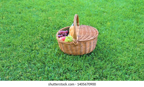 
Wicker Picnic Basket With White And Black Grapes And Wine On Green Grass Outside In Summer Park, No People