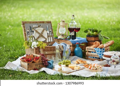 Wicker Picnic Hamper With Assorted Fresh Food, Infused Water And Wine On A Rug Spread Out On The Green Grass In A Park