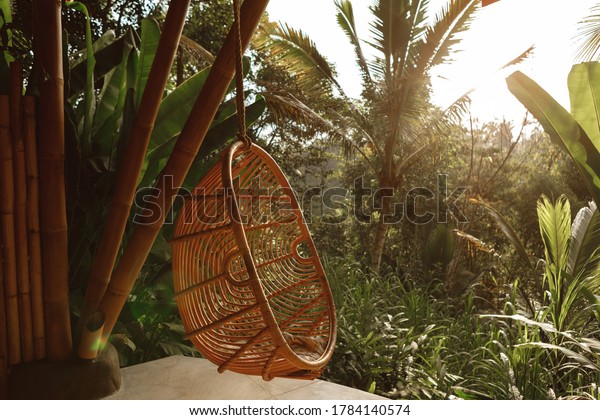 Wicker rattan hanging chair on wooden bamboo\
terrace in the jungle, nature view. Rattan lounge hanging chair at\
the balcony with green nature\
background
