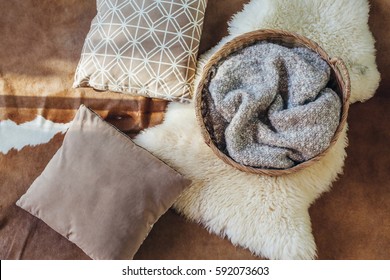 Wicker Storage Basket With Woolen Blanket Inside And Cushions On Sheep Carpet, Top View From Above. Natural And Organic Interior Decor.